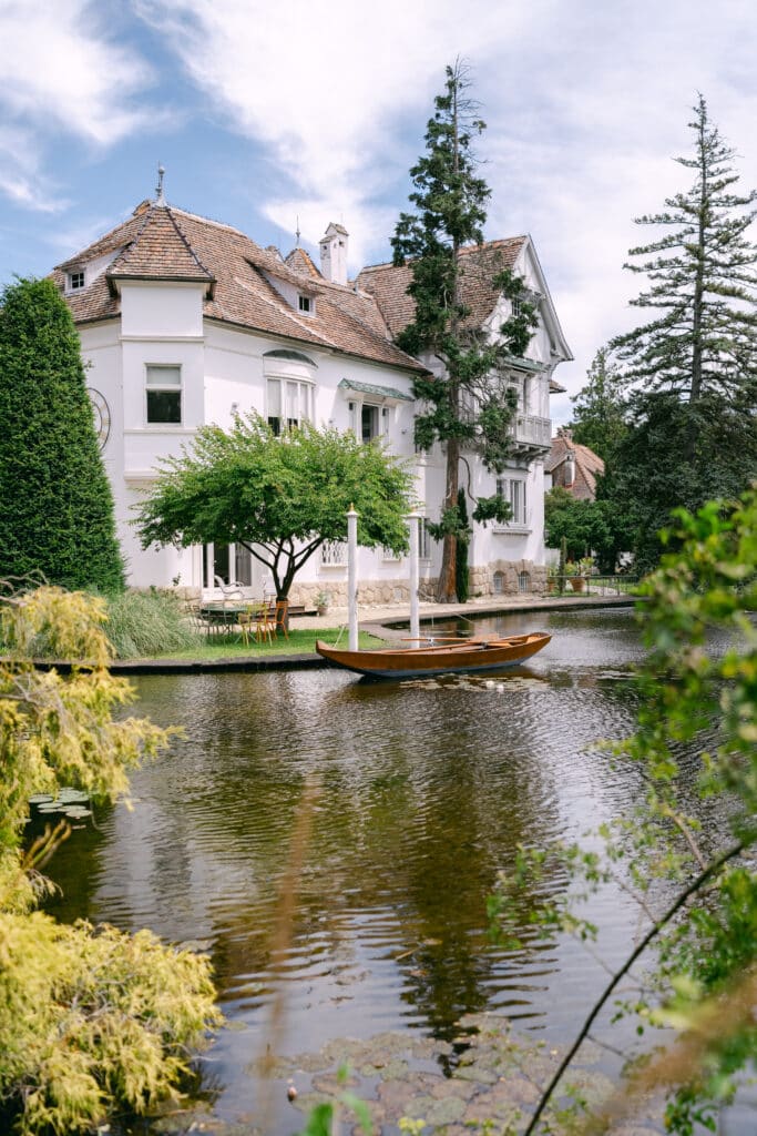 Blick auf Schloss Schönau mit einem kleinen Holzboot auf dem Teich im Vordergrund und üppigem Grün