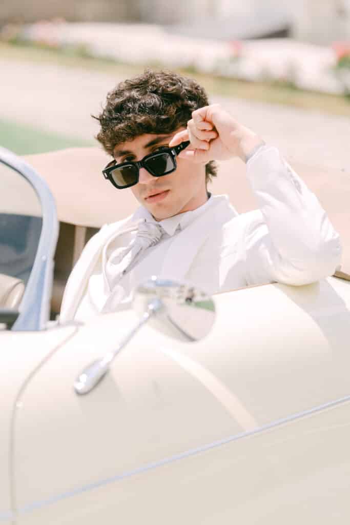 Bräutigam mit Sonnenbrille im Oldtimer vor der Villa Mosconi Bertani