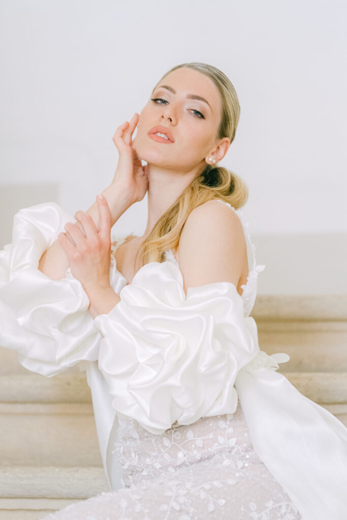 Braut im Couture-Kleid mit voluminösen Ärmeln auf einer Steintreppe