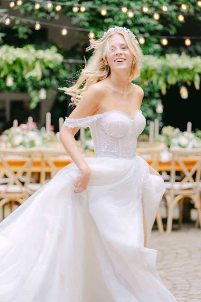 Lachende Braut läuft im Hochzeitskleid unter Lichterkette durch Gartenlocation