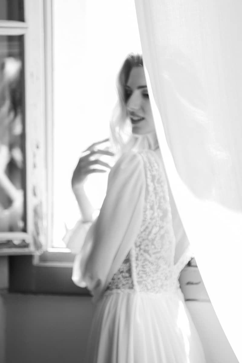 Artistic black and white portrait of a bride by the window in a flowing dress at Villa Mosconi Bertani in Vienna, captured by die hochzeitsfotografen.